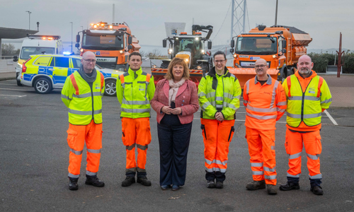 Transport Secretary Fiona Hyslop poses for a photo with colleagues from our road operating teams, who are dressed in hi-vis clothing. Resilience vehicles in the background.
