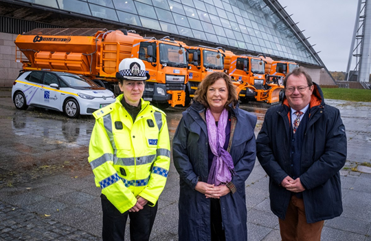 Transport Minister Fiona Hyslop poses for a photo with Chief Superintendent Hilary Sloan, head of Road Policing, and Met Office Markets Director Ian Cameron. They are standing in front of four orange gritters.